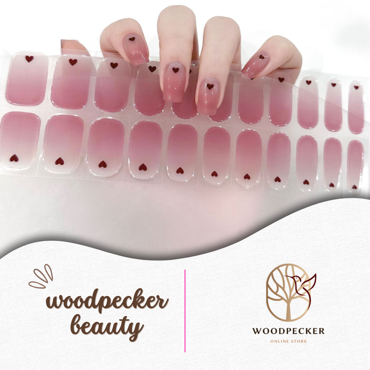 Hand holding a full set of pink gradient nail stickers with small heart designs from Woodpecker Beauty