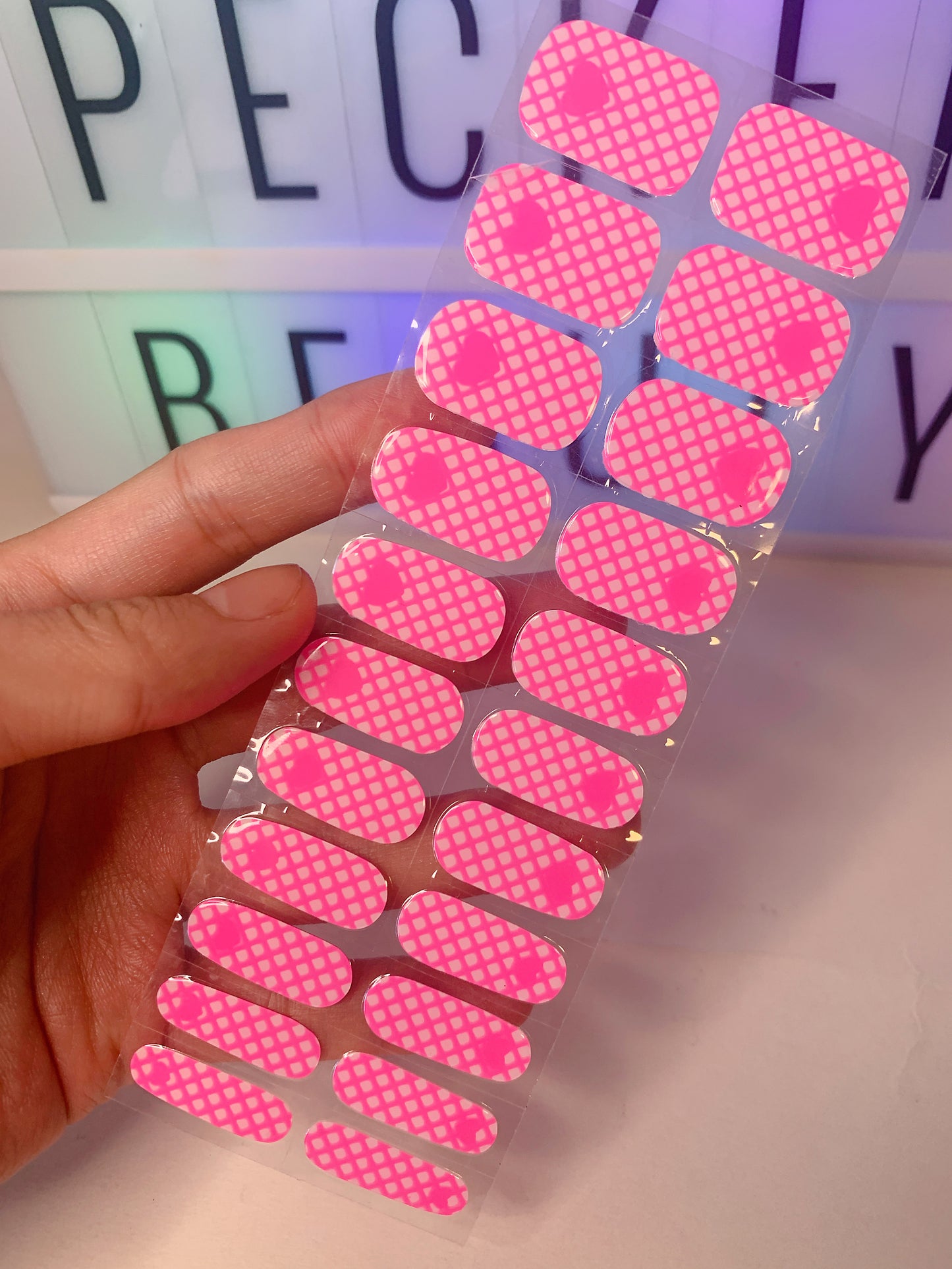 Hand holding a set of pink grid heart nail wraps