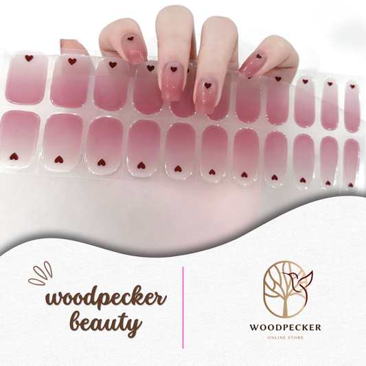 Hand holding a full set of pink gradient nail stickers with small heart designs from Woodpecker Beauty

