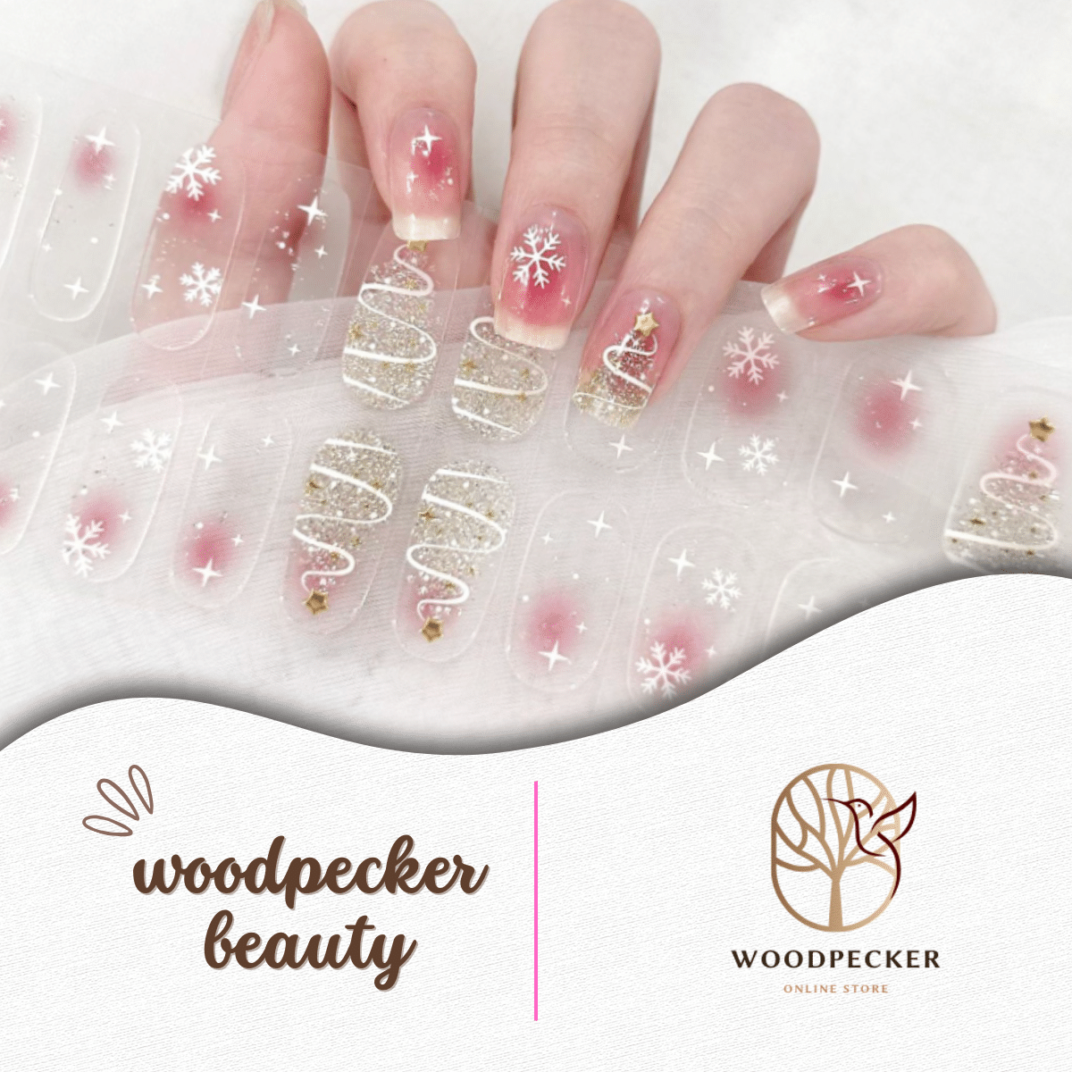 Hand wearing Christmas-themed nail stickers with snowflakes, gold glitter Christmas trees, and sheer pink base.
