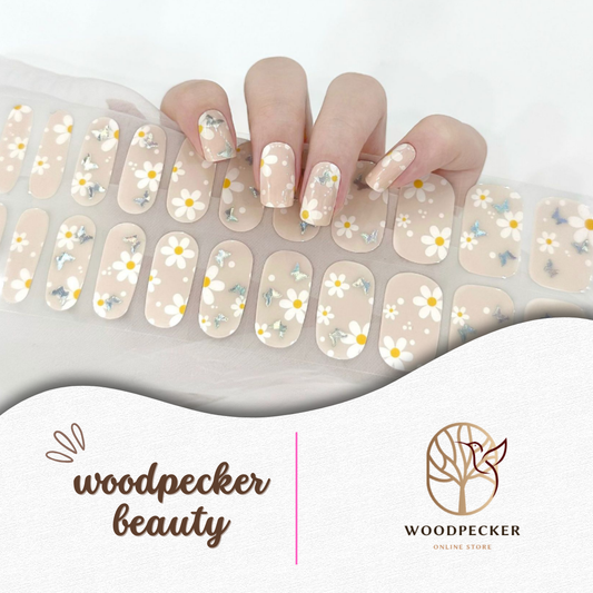 Hand with semi-cured gel nail wraps featuring white daisy flowers on a nude transparent base, UV lamp required
