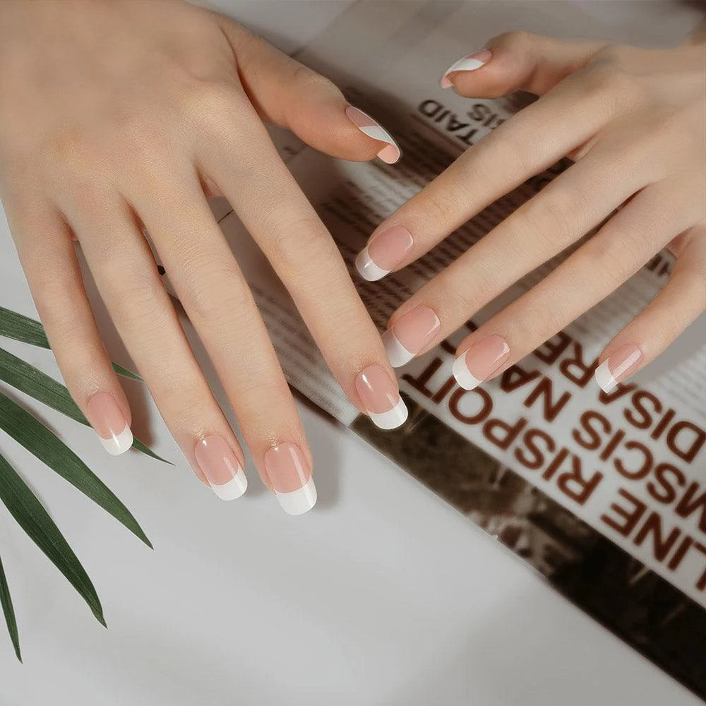 Hands showing classic French tip nail stickers with a sheer pink base and crisp white tips.
