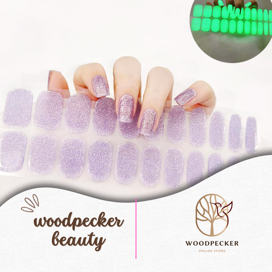 Hand with semi-cured gel nail wraps in glitter lavender color that glow green in the dark, UV lamp required