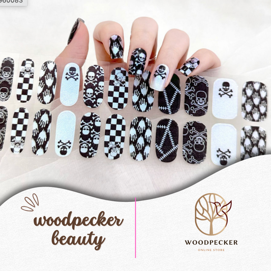 Hand with punk-inspired semi-cured gel nail wraps featuring skulls, bones, checkerboard, and gothic stitching, UV lamp required