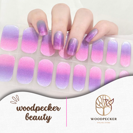 Hand holding a sheet of purple to pink gradient nail wraps with semi-transparent shimmer finish