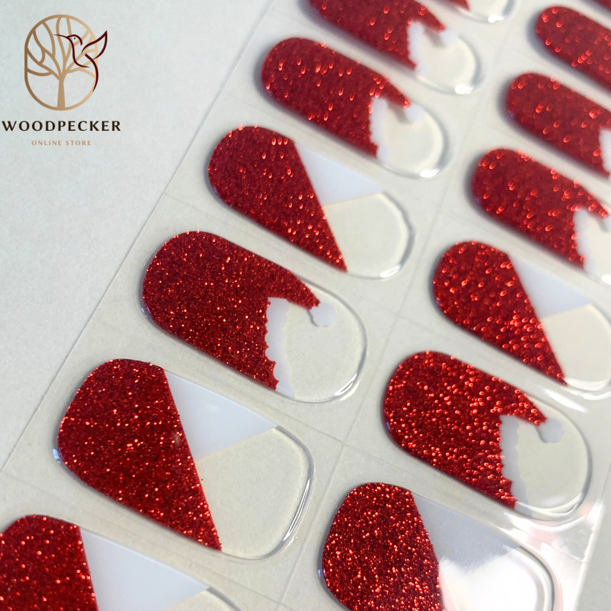 Close-up of red glitter Santa hat nail wraps with white tips and transparent background.
